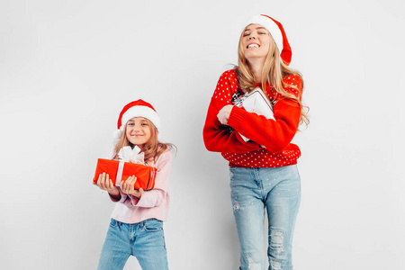 震惊的妈妈和女儿穿着圣诞帽和毛衣庆祝新年，手里拿着白色背景的礼物。