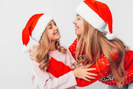 妈妈和女儿戴着圣诞老人的帽子，穿着圣诞毛衣互相拥抱。 在白色的背景上。 强大家庭的概念。