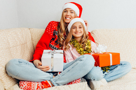 圣诞老人帽子里快乐的妈妈和女儿坐在沙发上看着他们的圣诞礼物。 圣诞节概念