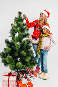 妈妈和女儿戴着圣诞老人的帽子，用白色的背景装饰圣诞树