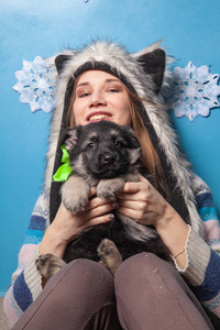 漂亮的女人戴着毛皮冬帽，抱着一只可爱的牧羊犬，在蓝色的背景上微笑