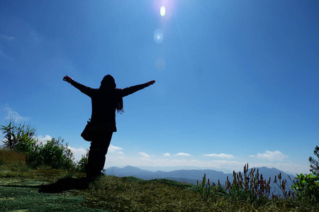 游客女人穿着毛衣站在悬崖上，举起双手，望着天空和山，自由和旅游的概念。