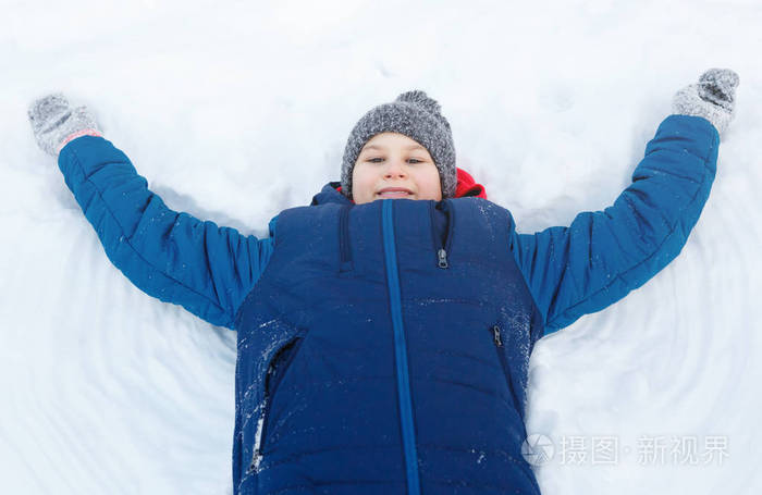 可爱的小男孩穿着蓝色夹克玩雪，玩得开心，微笑。少年举起双手，在冬季公园的雪地上做数字。积极的生活方式，冬季活动，户外冬季游戏，雪