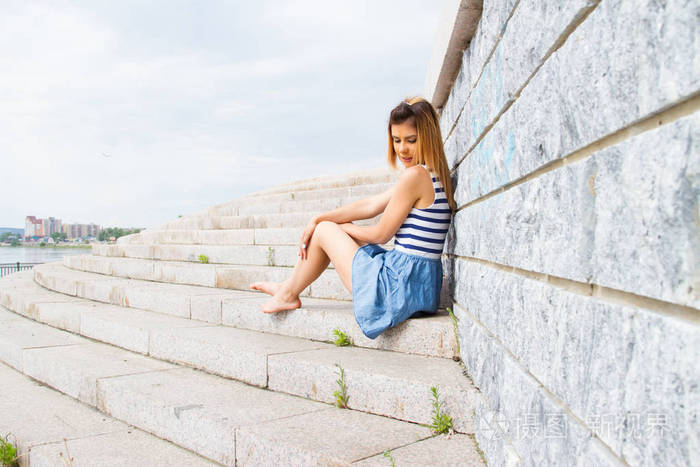 年轻女孩坐在靠在石墙上的混凝土楼梯的台阶上