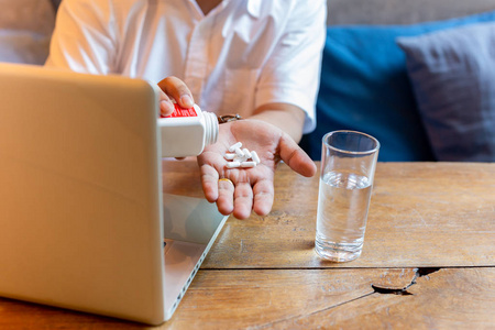 一个人拿着一杯水和笔记本电脑在木桌上吃药