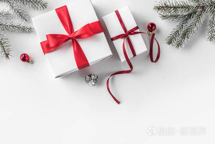 创意框架由圣诞杉枝在白纸背景上与红色装饰松果。 圣诞节和新年主题。 平躺式顶部视图