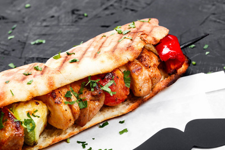 三明治从新鲜皮塔面包与鱼片烤鸡和蔬菜在黑暗的木制背景。 什什利克或什什烤肉串。 健康午餐