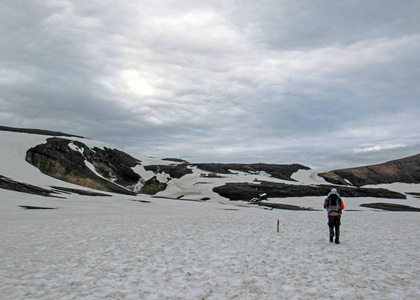 徒步旅行者独自进入野外欣赏火山景观与流纹岩山脉和雪与沉重的背包。 旅行生活方式冒险流浪概念暑假户外