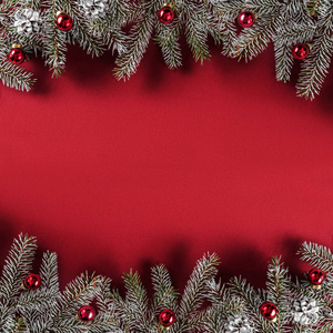 创意布局框架由圣诞杉木树枝松果红色装饰在红纸背景上。 圣诞节和新年主题。 平躺式顶部视图