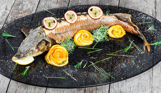 烤鲟鱼与迷迭香柠檬和激情水果在盘子上的木制背景关闭。 健康的食物。 上面的风景。 俄罗斯传统。 顶部视图