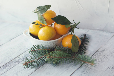 橘子柑桔，叶子放在白色的盘子里，放在木制的背景上，上面有圣诞树皮