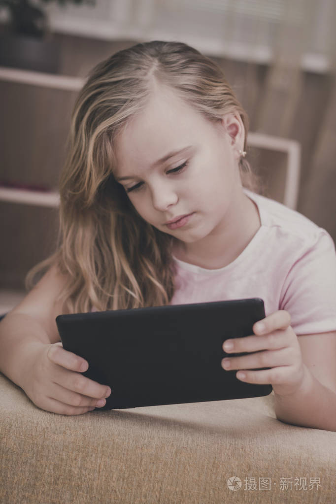 漂亮的女孩在家里玩平板电脑的技术概念.