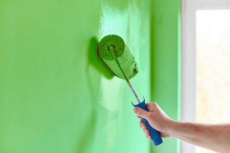 男手画墙与油漆滚筒。 油漆公寓用绿色油漆翻新