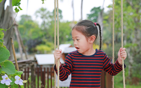 小亚洲女孩的肖像，在自然公园里玩耍和坐在秋千上。