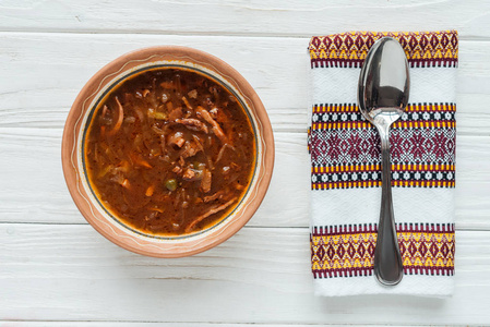 白色木制背景上用勺子和刺绣毛巾制作的美味传统混合肉汤的顶部景观