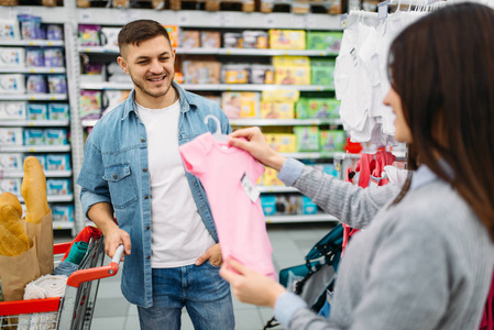 幸福的夫妇在超市的家庭购物中买童装。 顾客在商场购买儿童用品