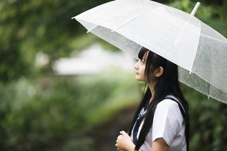 亚洲女孩的肖像,带着雨伞在雨中的自然人行道上散步照片