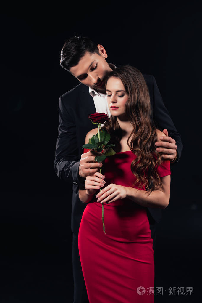一个英俊的男人拥抱着一个穿着红色衣服抱着玫瑰的漂亮女人