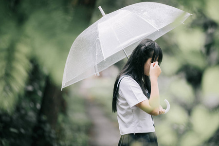 亚洲女孩的肖像，带着雨伞在雨中的自然人行道上散步