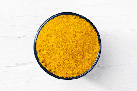 咖喱香料粉末在圆形碗白色木制背景视图直接从上面.照片