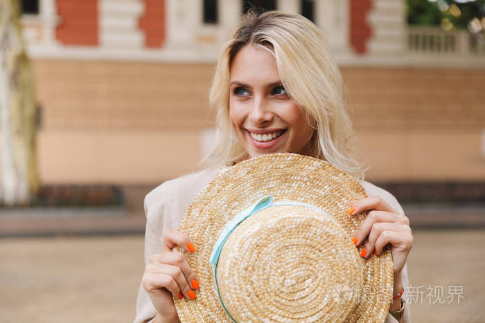 一个快乐的年轻女人走在户外手拿帽子的形象.