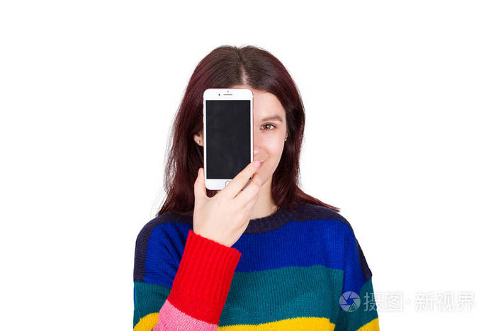 美丽的年轻女子穿着五颜六色的毛衣用她的手机空屏遮住半张脸积极的