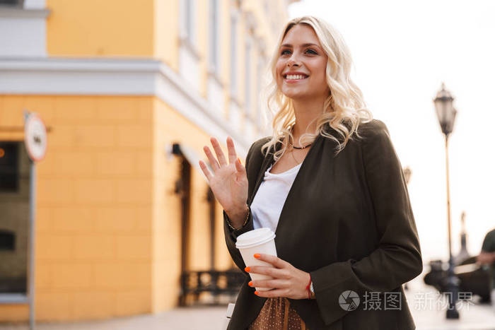 欧洲女人穿着夹克，拿着外卖的咖啡在纸杯里走过城市街道的形象