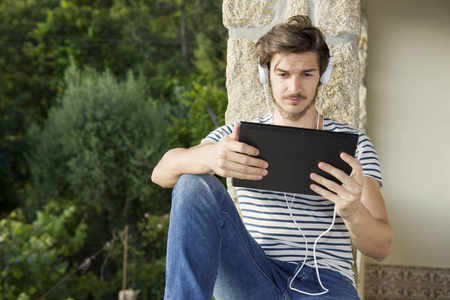 年轻人带着平板电脑和耳机在户外听音乐放松
