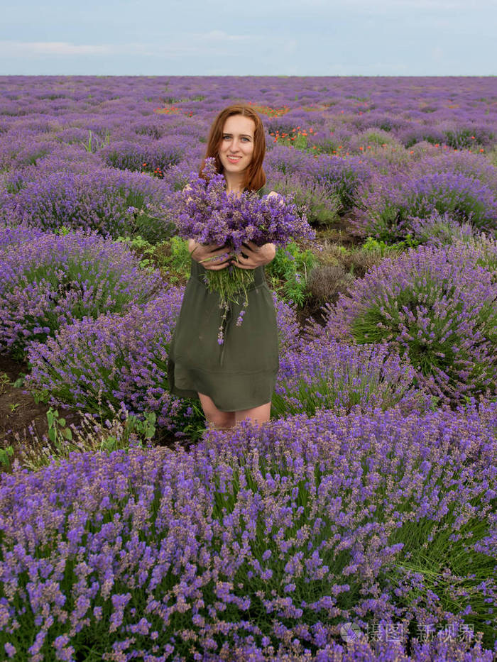 年轻的女孩手里拿着一束花在薰衣草的田野里摆姿势
