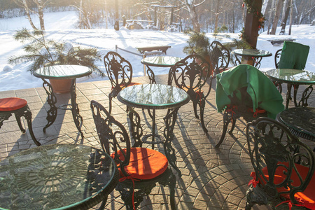 在餐厅露台上铸造铁椅和桌子, 配有枕头和毯子。冬天的风景是寒冷的树木, 白雪和蓝天。公园里阳光下宁静的冬季自然