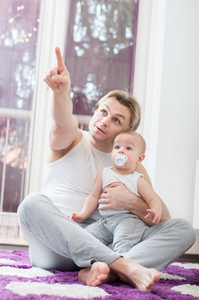 快乐的父亲坐在地板上和他的小男孩玩。 手指指向。