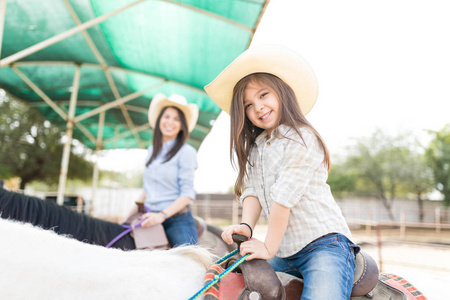 幸福的小女孩戴着帽子，在农场和母亲骑马时的肖像