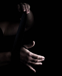 男人用黑色纺织绷带包扎他的手，用于运动黑色背景