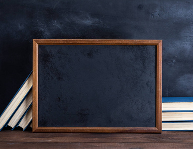 一张棕色木桌上的空黑粉笔画框和一叠书