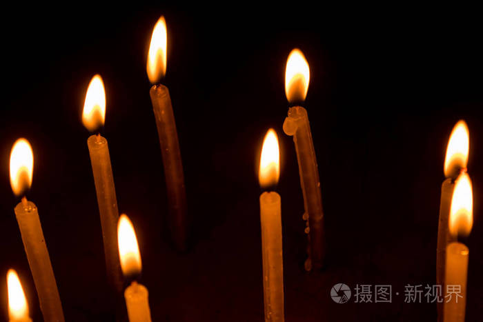 许多圣诞蜡烛在黑色的背景上夜间燃烧。 蜡烛火焰设置在黑色背景中隔离。 一组燃烧的蜡烛在黑暗中，有较浅的景深。 快关门。 自由空间