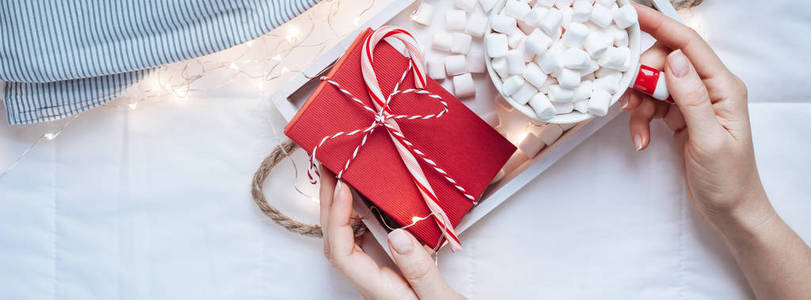 新年或圣诞节平躺顶景，上面有热可可咖啡巧克力和棉花糖杯，圣诞节庆祝活动，红色礼物盒，放在木制托盘床上，上面有灯和女人的手长宽的横