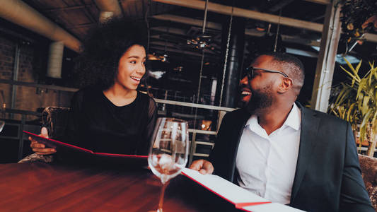 非裔美国人夫妇在餐馆约会。 浪漫的情侣恋爱约会。 欢快的男人和女人在餐馆里点菜。 浪漫的概念。 周年纪念。 日期。 爱。