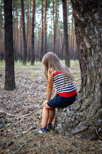 夏天，小美丽的女孩坐在松林里的一个树桩上。