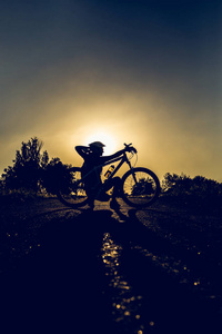 夏天日落时骑自行车的女孩的剪影。