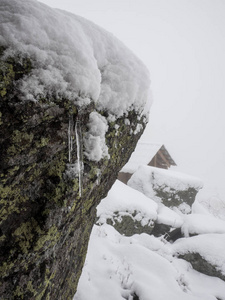 暴风雪中岩石上的冰柱。 背景下有雪堆的房子的屋顶