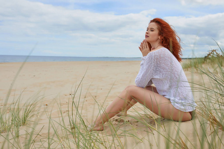 红发女孩独自坐在空旷的波罗的海海滩上