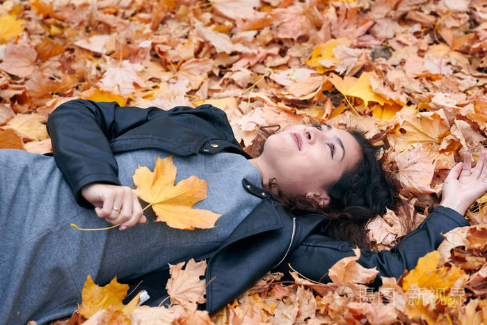 漂亮的女人躺在秋天的公园里落叶上秋天的美丽景色