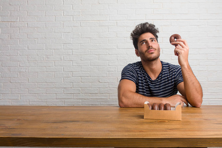 年轻英俊自然的男人坐在桌子上,抬头看着一些有趣的事情,有一个想象的