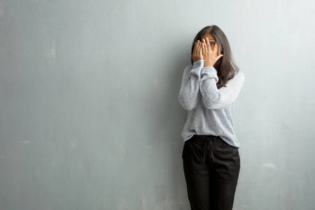 年轻的印度女人靠在一堵破旧的墙上,感到担心和害怕,看着,捂着脸,恐惧