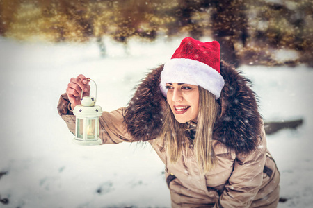 戴着圣诞帽的年轻女子，在美丽的冬日里，在户外举着圣诞灯笼