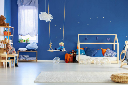蓝色的墙壁，金色的星星，时尚的斯堪的纳维亚儿童房，木制的房子，形状的床，枕头。