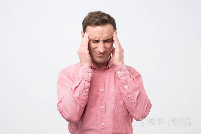 英俊的欧洲男人显示他的头有多疼, 经历疼痛, 看起来精疲力竭