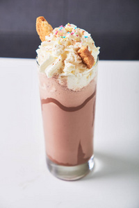 在咖啡馆的桌子上，在玻璃中加入冷巧克力奶昔。夏日甜饮料。