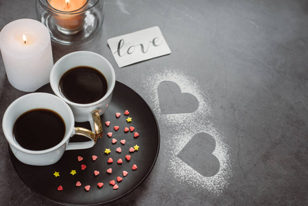 情人节。两杯咖啡蜡烛和心在黑暗的背景。 敬所有情人的日子
