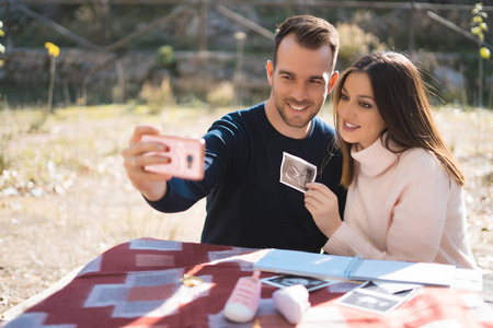 孕妇和她丈夫在外面用超声波图像自拍。 怀孕亲子准备和期望概念。